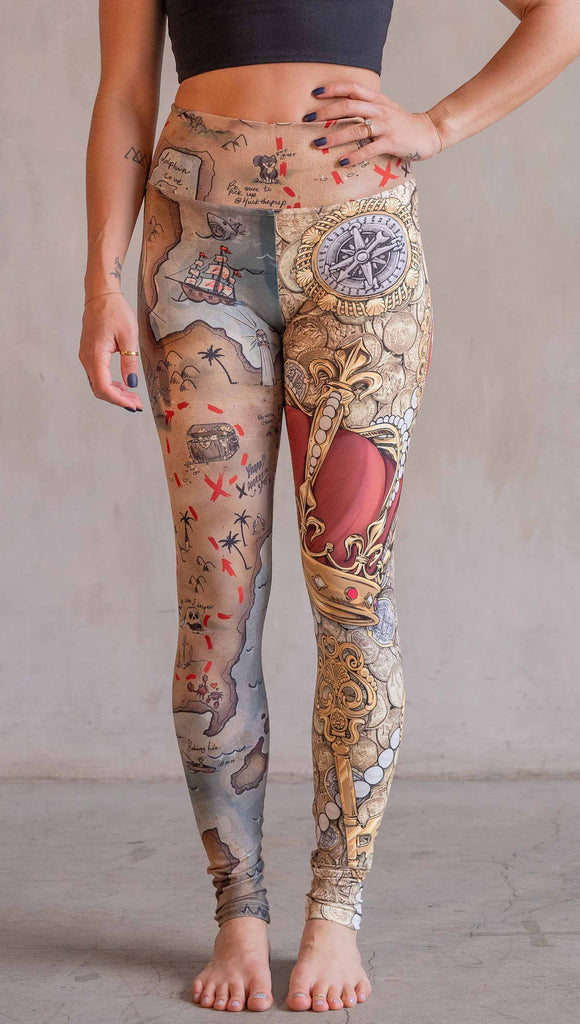 Model wearing WERKSHOP Booty Mashup Leggings. The wearer's right leg is printed with vintage inspired, hand drawn, treasure map artwork and the left leg is golden treasure with a kings royal crown, keys and pearls: everything you'd expect to find inside a pirates treasure.