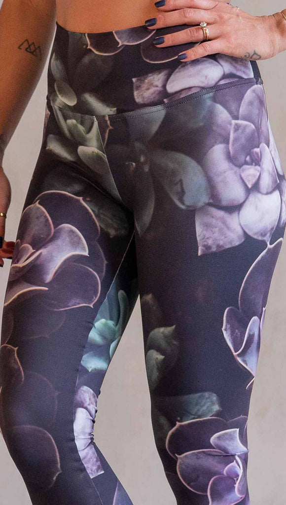 Model wearing WERKSHOP Midnight Garden Athleisure Leggings. The artwork on the leggings is printed with succulents in dark romantic colors of purple with small pops of teal