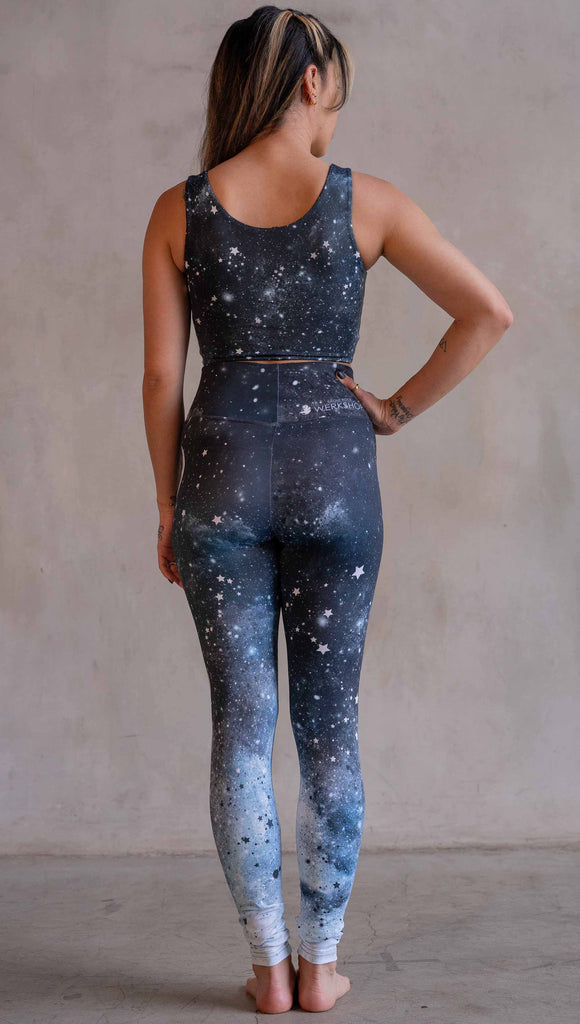 Model wearing WERKSHOP Moon Phases Athleisure Leggings. The leggings feature the phases of the moon down the wearer's left leg over a starry blue galactic background. All 12 zodiac constellations are sprinkled throughout the background of the design.