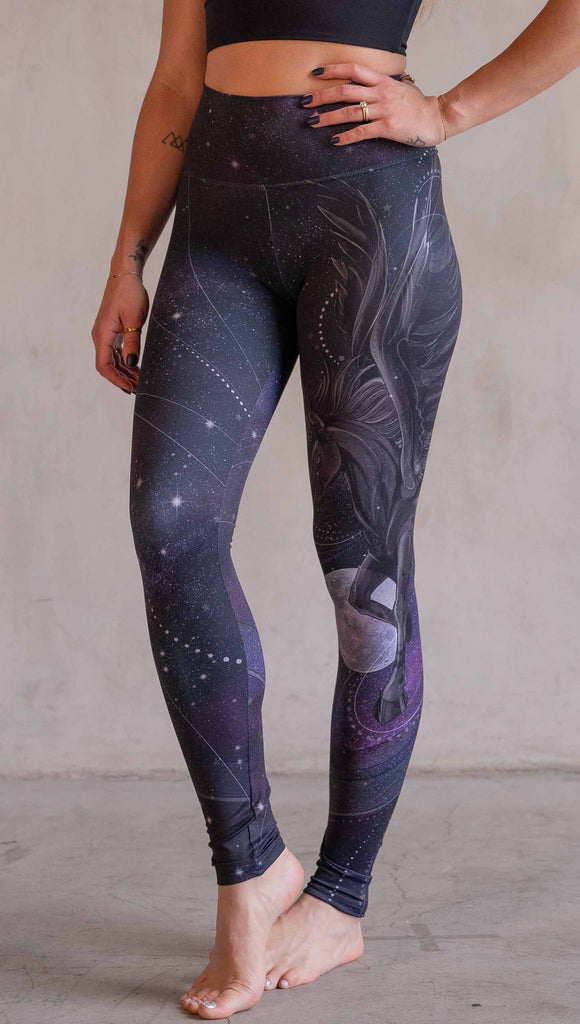 Model wearing WERKSHOP Nightmare Athleisure leggings. The artwork on the leggings features a pegasus flying through a purple galactic sky on the wearers left leg with swirls and a full moon just below the left knee.