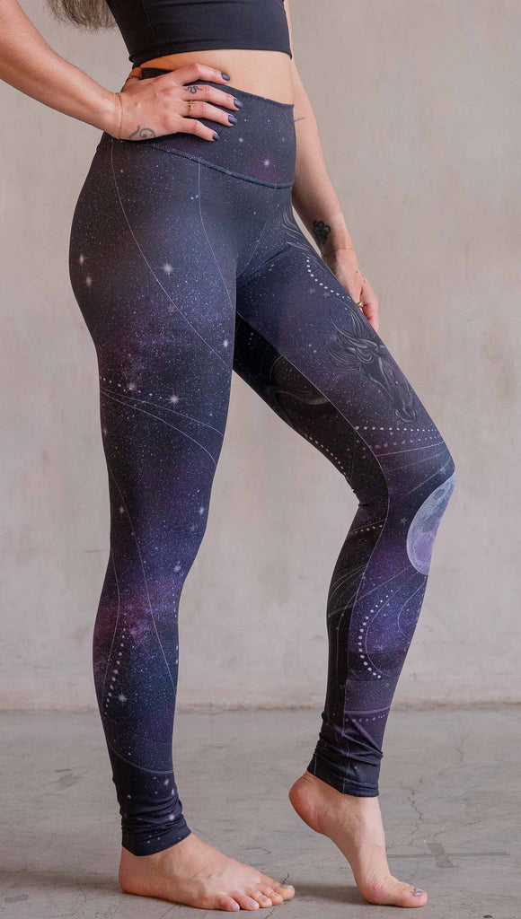 Model wearing WERKSHOP Nightmare Athleisure leggings. The artwork on the leggings features a pegasus flying through a purple galactic sky on the wearers left leg with swirls and a full moon just below the left knee.