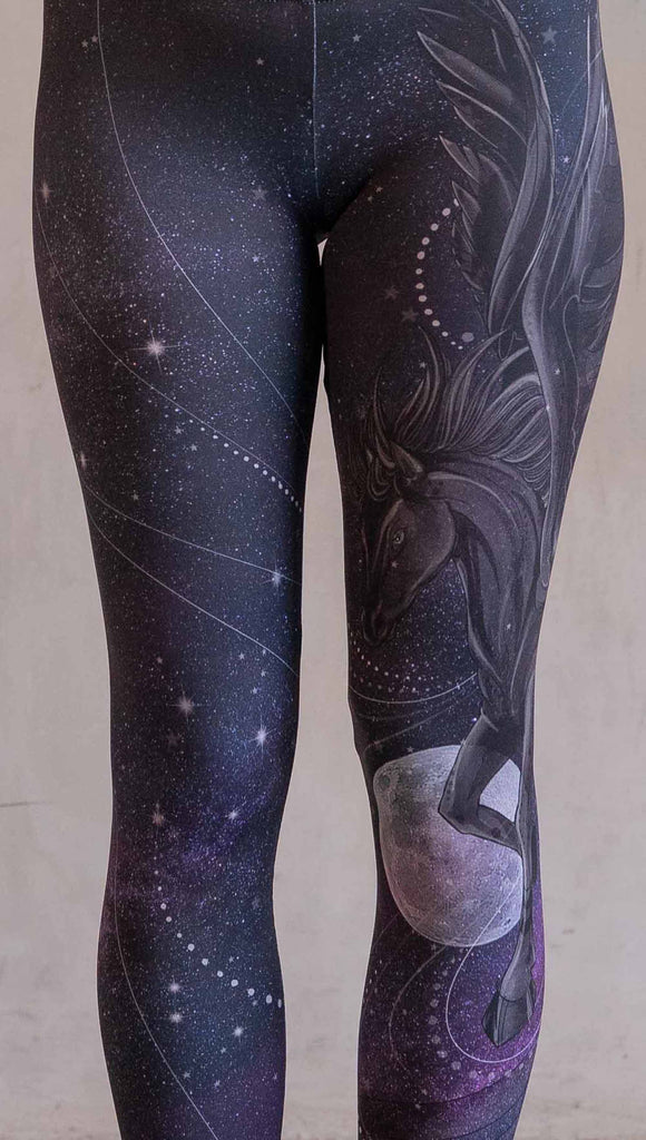 Model wearing WERKSHOP Nightmare Athleisure leggings. The artwork on the leggings features a pegasus flying through a purple galactic sky on the wearers left leg with swirls and a full moon just below the left knee.