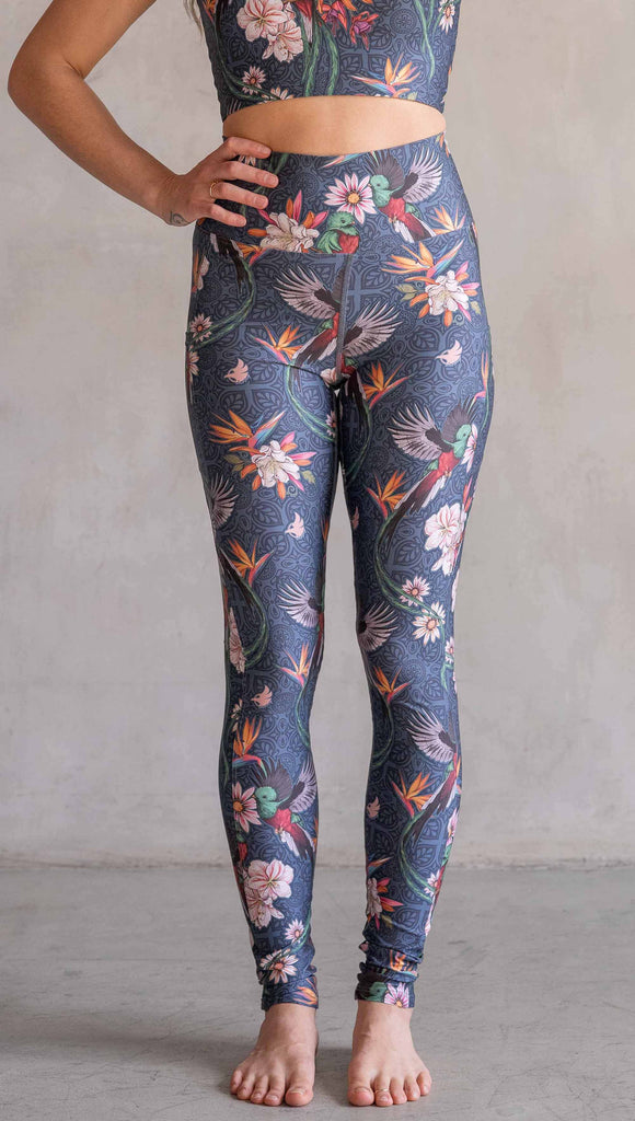 Model wearing WERKSHOP Quetzal Featherlight Leggings. The leggings are printed with with original quetzal artwork with clusters of tropical flowers and birds of paradise over a blue background. The featherlight leggings have pockets.