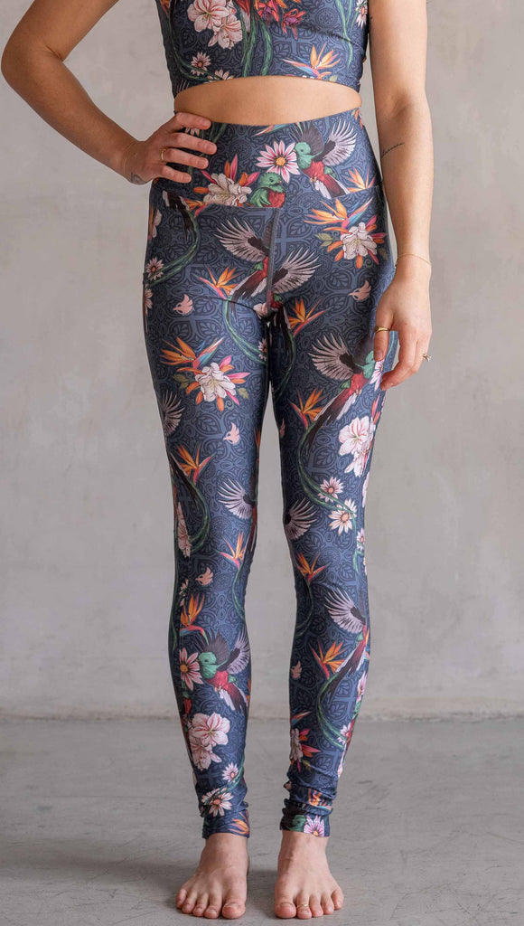 Model wearing WERKSHOP Quetzal Featherlight Leggings. The leggings are printed with with original quetzal artwork with clusters of tropical flowers and birds of paradise over a blue background. The featherlight leggings have pockets.