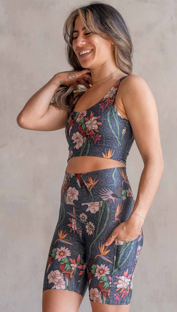 Model wearing WERKSHOP Quetzal Featherlight Bicycle length shorts. The shorts are printed with with original quetzal artwork with clusters of tropical flowers and birds of paradise over a blue background. The featherlight shirt have pockets.