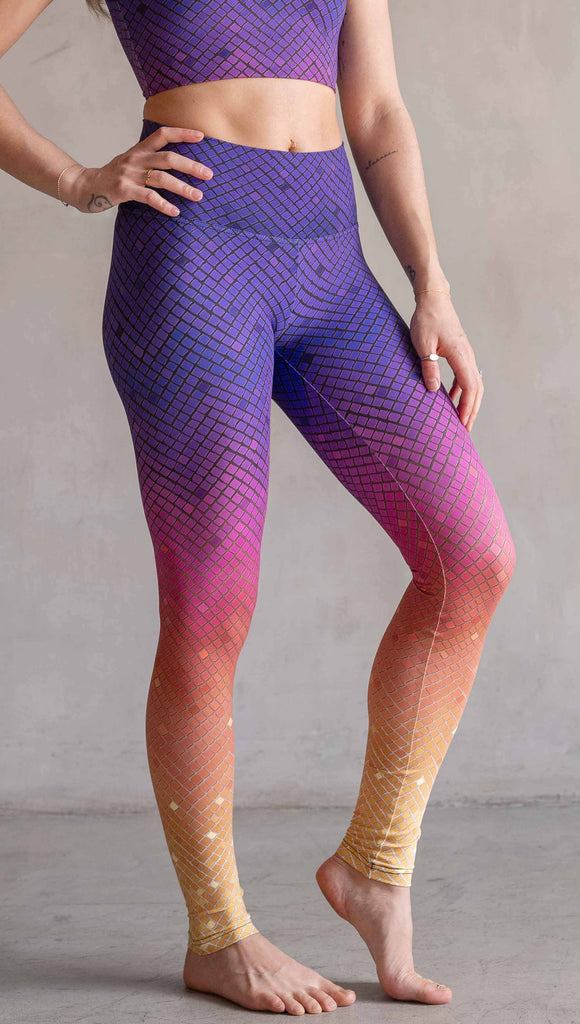 Model wearing WERKSHOP Rainbow Mosaic Athlesiure Leggings and matching top. The leggings are printed with what look like tiny mosaic tiles in an ombre effect from purple at the waistband, to pink at the knee ... then coral and a soft warm yellow at the leg opening.