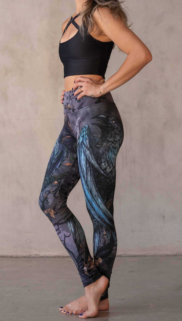 Girl wearing WERKSHOP "Raven" athleisure leggings. The artwork on the leggings feature a raven perched on a branch looking into the moonlight with pops of blue glistening from his feathers. He is framed by autumn leaves over a very spooky night sky.