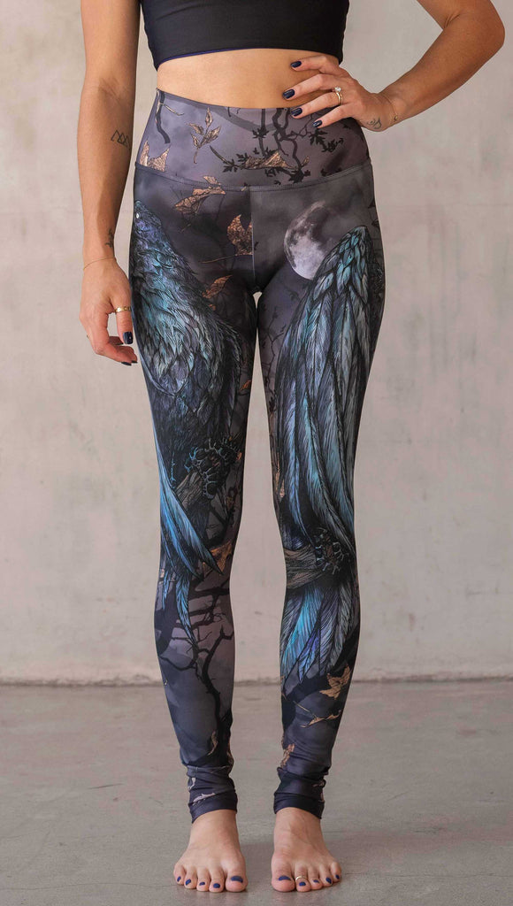 Girl wearing WERKSHOP "Raven" athleisure leggings. The artwork on the leggings feature a raven perched on a branch looking into the moonlight with pops of blue glistening from his feathers. He is framed by autumn leaves over a very spooky night sky.