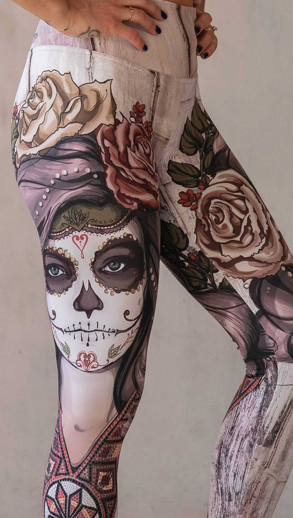 Girl wearing WERKSHOP "Remix" SugarSkull Athelisure leggings. The artwork printed on the leggings features a girl wearing Dia De Los Muertos makeup with a crown of roses and a beaded necklace with a romantic color woodgrain background.