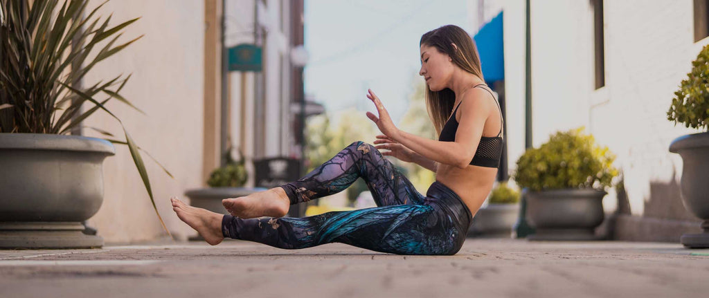 girl photographed in motion, sitting outside on the sidewalk, wearing WERKSHOP Raven Leggings in Triathlon Fabric