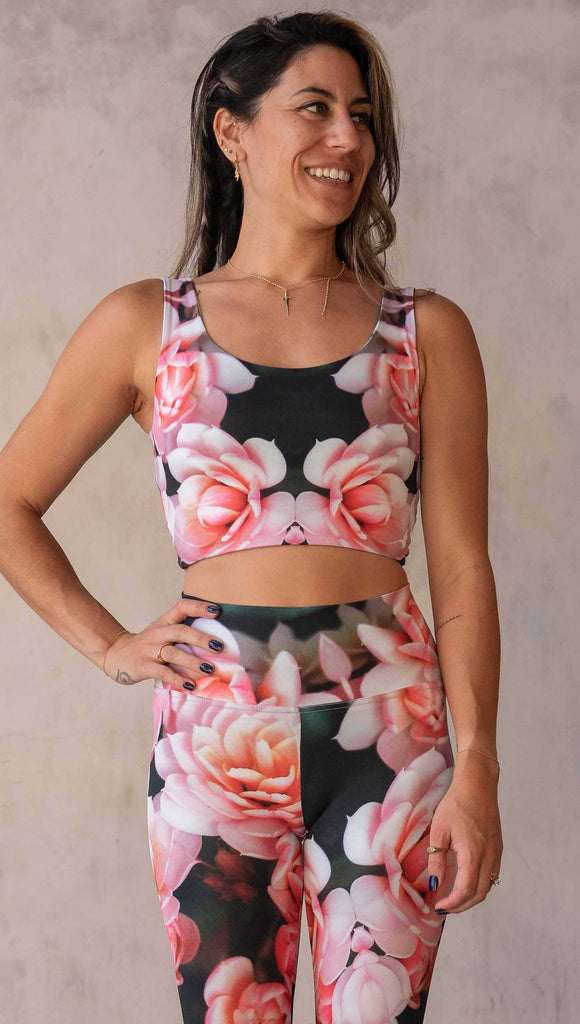 Girl wearing the WERKSHOP Reversible Artichoke and Rosaline Top. This image shows the Rosaline side. It has bright pink flowers with pops of bright peach/orange hues. The flowers are over a super dark blackish greenish background