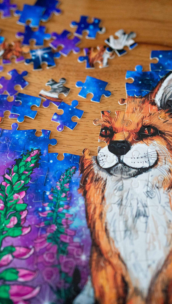 252 piece jigsaw puzzle featuring original artwork of a fox with foxglove in front of a galactic sky. A % of the proceeds benefit Save a Fox Rescue.