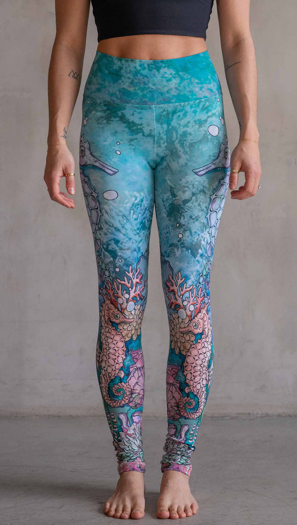 Model wearing WERKSHOP Seahorses Athleisure Leggings. The artwork on the leggings features pastel coloured seahorses and coral reef over an aqua/teal textured background.