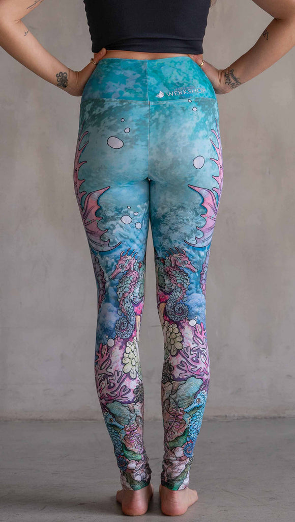 Model wearing WERKSHOP Seahorses Athleisure Leggings. The artwork on the leggings features pastel coloured seahorses and coral reef over an aqua/teal textured background.