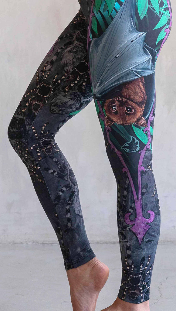 Model wearing WERKSHOP Spooky Season Set. The leggings feature an adorable fruit bat dangling upside down inside a tropical scene with a purple wreath of thorns. The background is a distressed dark gray brushstroke texture. (This version of the artwork has no rats)