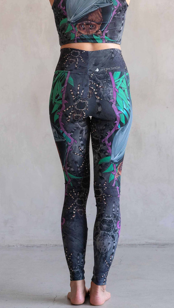 Model wearing WERKSHOP Spooky Season Set. The leggings feature an adorable fruit bat dangling upside down inside a tropical scene with a purple wreath of thorns. The background is a distressed dark gray brushstroke texture. (This version of the artwork has no rats)