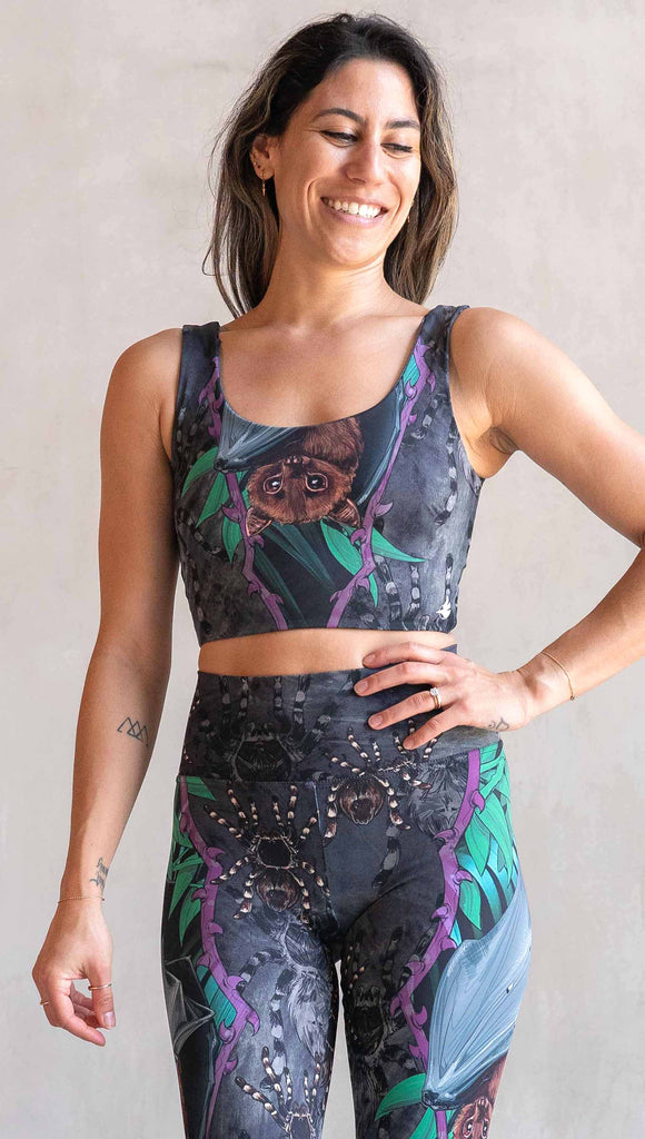 Model wearing WERKSHOP Spooky Season Set. The reversible top features an adorable fruit bat dangling upside down inside a tropical scene with a purple wreath of thorns. The background is a distressed dark gray brushstroke texture. (This version of the artwork has no rats, but does have scattered tarantulas)