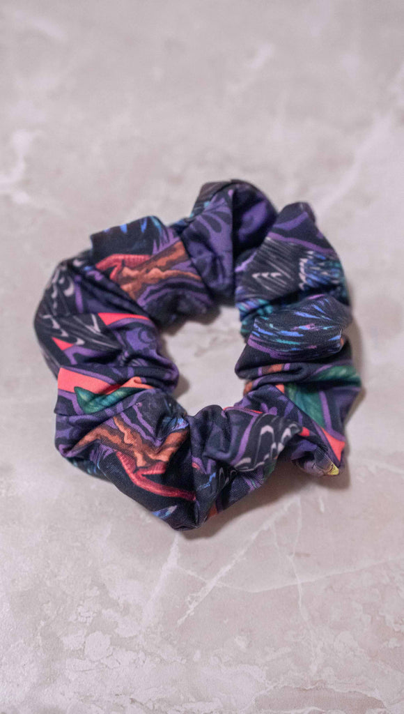 WERKSHOP Starlings hair scrunchie. The scrunchie is mostly a deep purple/blue with little bright pops of coral and green.