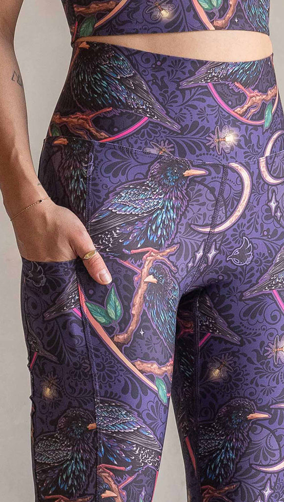 Zoomed in view of model wearing WERKSHOP Starlings EnviSoft bell bottom pants with pockets. The fabric is printed with original artwork by our Female Founder, Chriztina Marie. Featuring European Starlings perched on a branch near a crescent moon and fireflies. The colors are warm purples with pops of pink, gold and green.