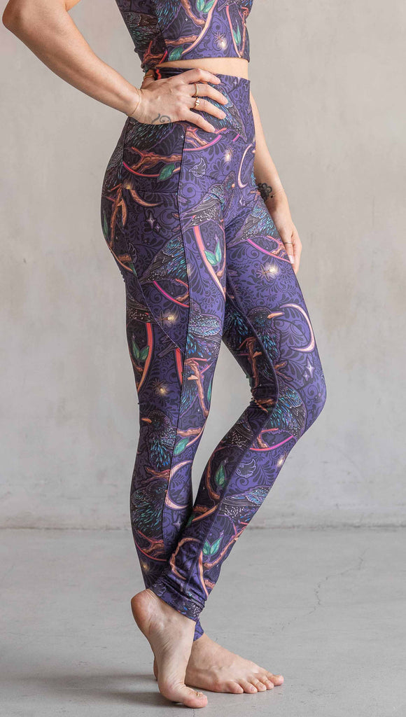 Side view of model wearing WERKSHOP Starlings EnviSoft leggings with pockets. The fabric is printed with original artwork by our Female Founder, Chriztina Marie. Featuring European Starlings perched on a branch near a crescent moon and fireflies. The colors are warm purples with pops of pink, gold and green.