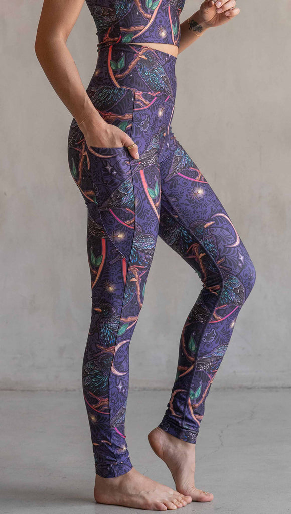 Side view of model wearing WERKSHOP Starlings EnviSoft leggings with pockets. The fabric is printed with original artwork by our Female Founder, Chriztina Marie. Featuring European Starlings perched on a branch near a crescent moon and fireflies. The colors are warm purples with pops of pink, gold and green.