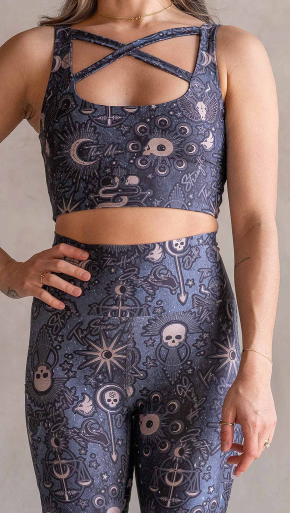 Model wearing WERKSHOP Tarot Bicycle Length Shorts. They are high waist and feature pockets on both legs. The blue/tarot artwork has skulls, snakes, moons and the names of multiple popular tarot cards like "Strength, Lovers, Death and The Hanged Man”. The length of the shorts hit in the mid thigh, above the knee.