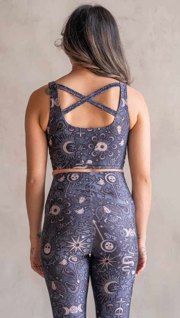 Front view of model wearing WERKSHOP Four-Way Reversible Top. The top has a tarot card themed artwork on a dark blue background on one side and a zodiac themed artwork on purple background on the opposite side. She is wearing it with the Blue side out and the X neckline detail in the back.