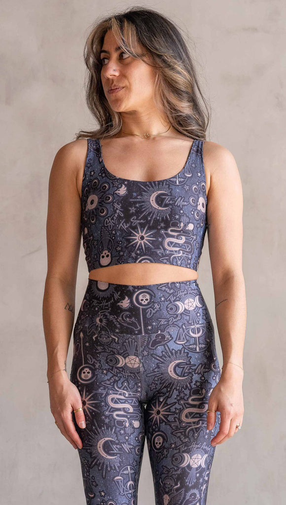 Front view of model wearing WERKSHOP Four-Way Reversible Top. The top has a tarot card themed artwork on a dark blue background on one side and a zodiac themed artwork on purple background on the opposite side. She is wearing it with the Blue side out and the X neckline detail in the back.