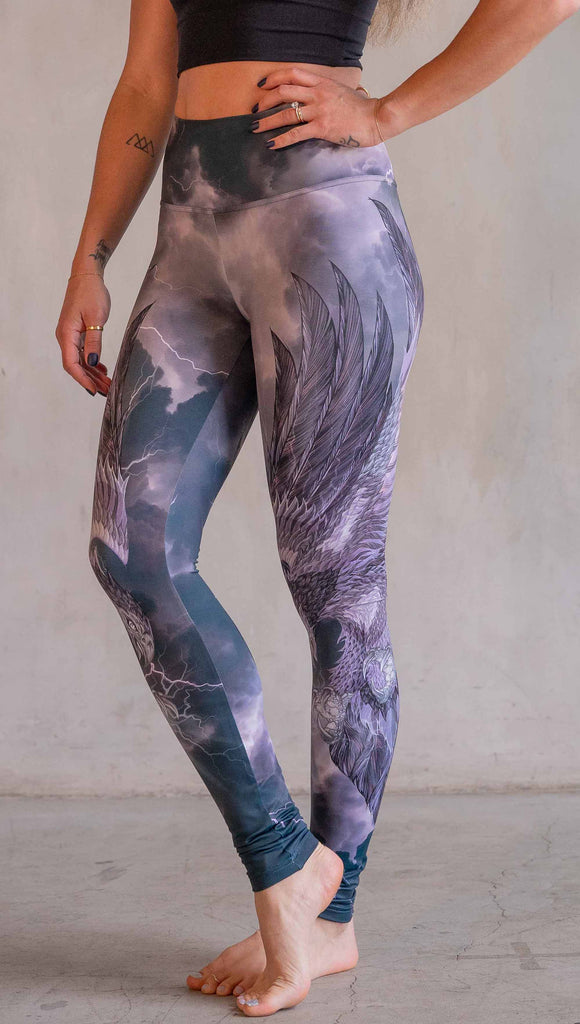 Model wearing WERKSHOP Thunderbird Athleisure Leggings. The artwork printed on the leggings features a thunderbird flying through a stormy sky with lightening. The leggings feature a closed colour pallete with all shades of purple.