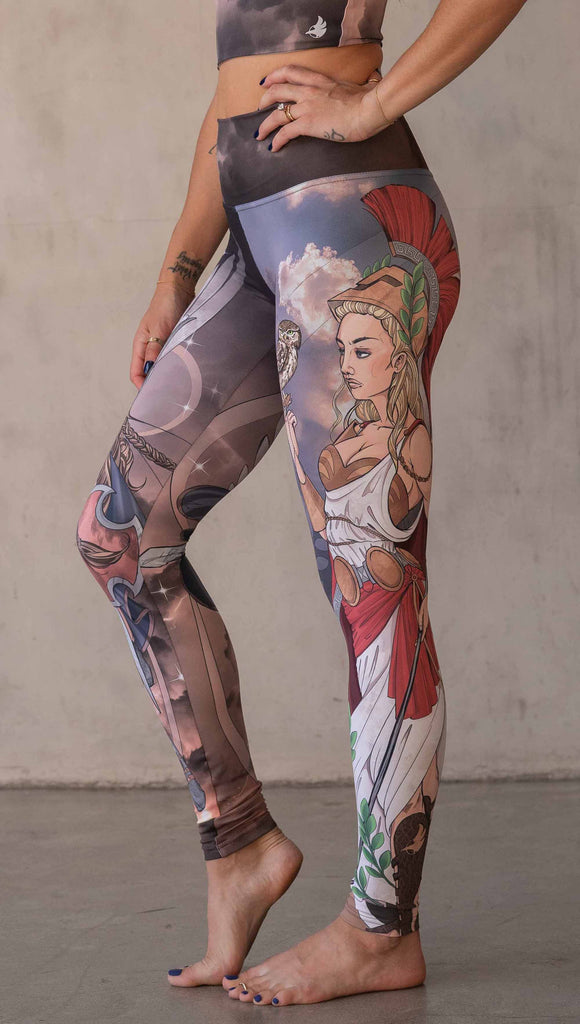 Model wearing WERKSHOP Valkyrie + Athena Mashup leggings. The leggings are printed with original artwork by Chriztina Marie. One leg features Athena, the goddess of war standing on a cliff’s edge. She is holding a spear with one hand and her owl with the other. The opposite leg features a Valkyrie warrior from Norse Mythology flying through a dark sky holding a shield and swords. Her hair is in braids and she is wearing armor and a viking helmet.