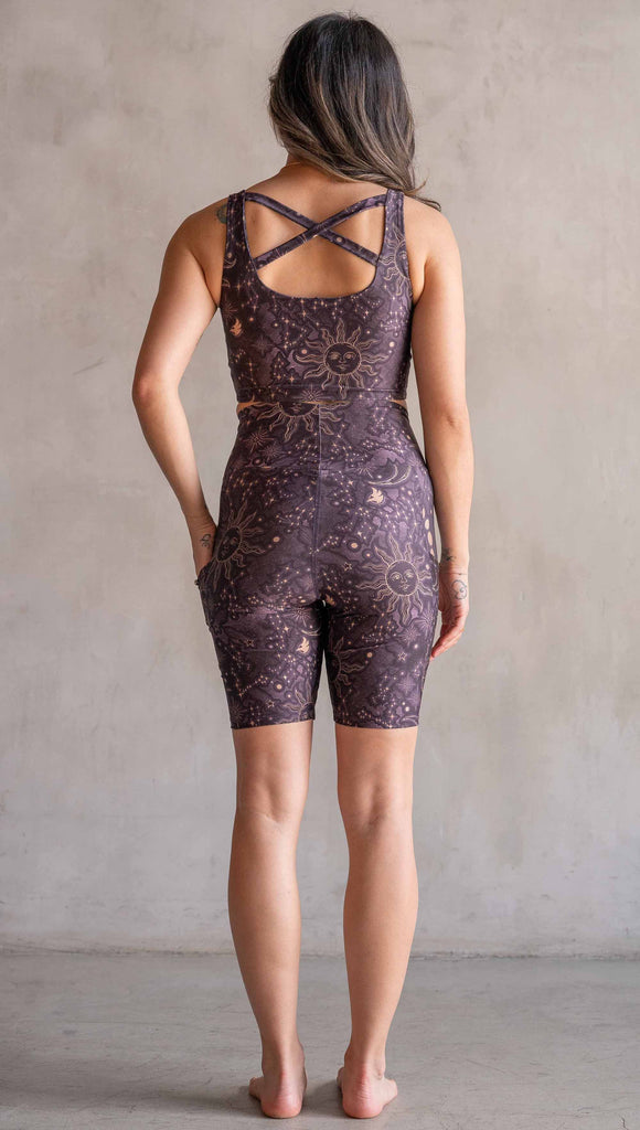 Model wearing WERKSHOP Zodiac Bicycle Length Shorts. They are high waist and feature pockets on both legs. The zodiac themed artwork shows a hand-drawn sun and moon with the moon phases, shooting stars and all 12 zodiac constellations in gold over a dark purple background. The length of the shorts hit in the mid thigh, above the knee.