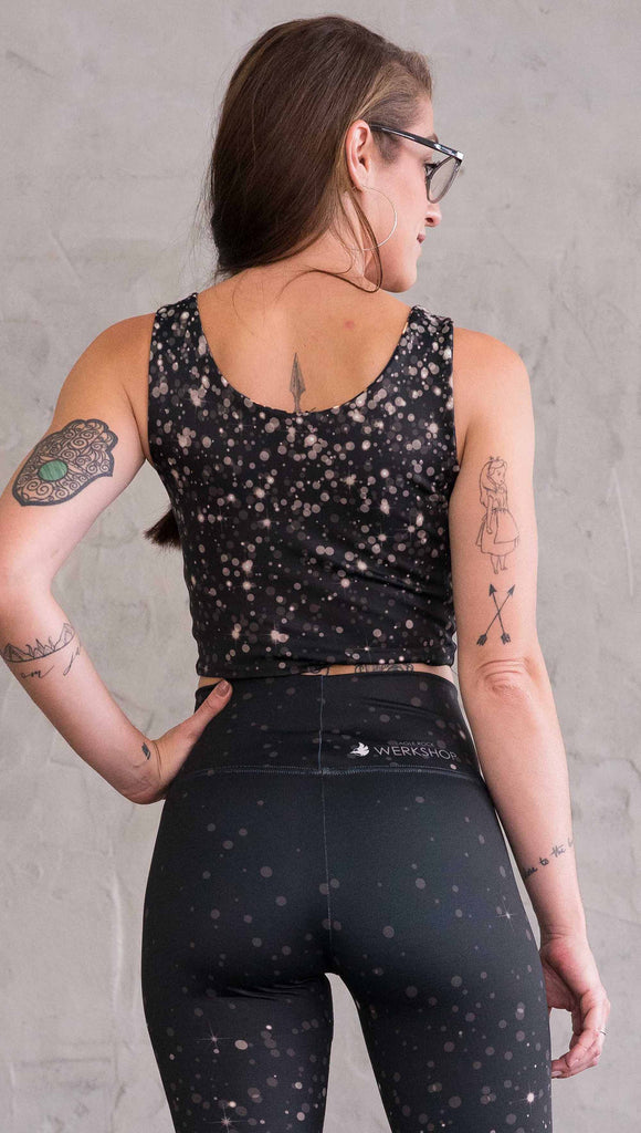 Back view of model wearing gold and silver sparkle WERKSHOP reversible top. With gold bokeh over blue-ish black background on one side and warm silver bokeh on black background on the opposite side.