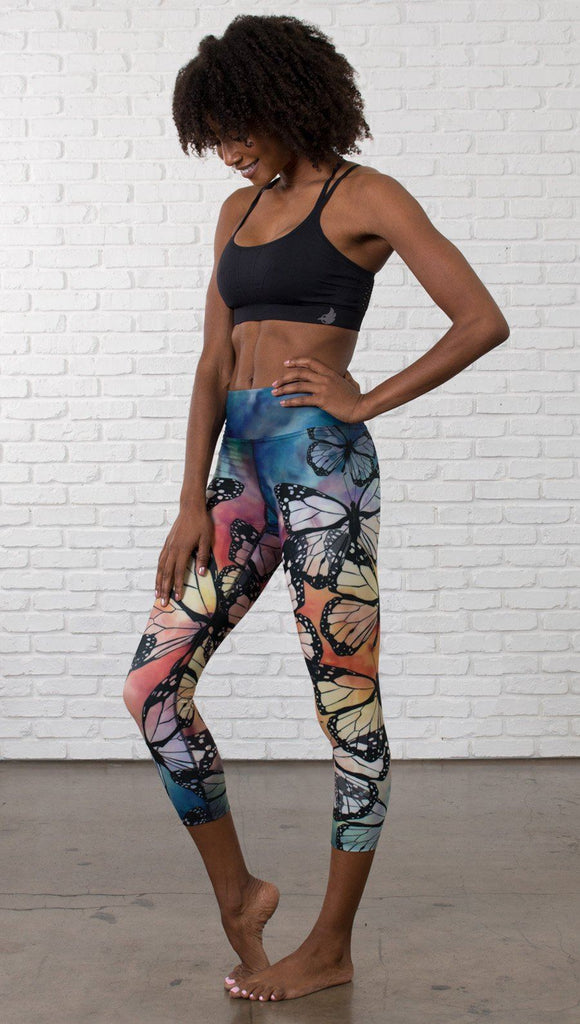 slightly turned front view of model wearing colorful butterfly themed printed capri triathlon leggings and sports top