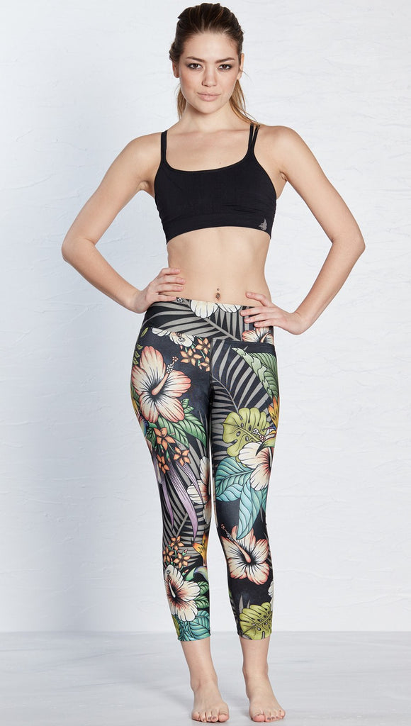 front view of model wearing printed capri leggings with tropical floral design and black background