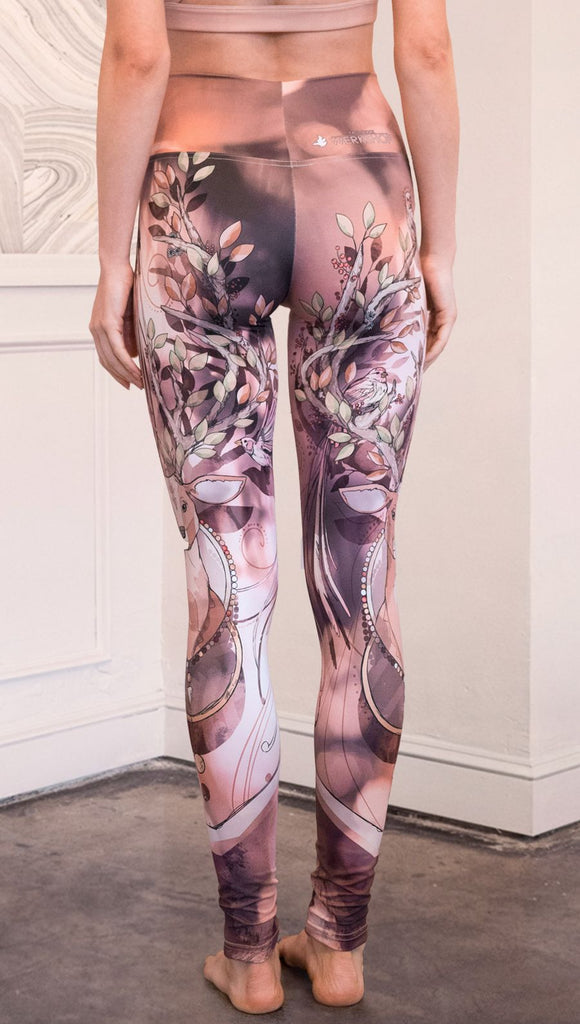 Back view of model wearing full length athleisure leggings with a deer on it. They are a purple and orange color with tree branches as the antlers and birds on the antlers