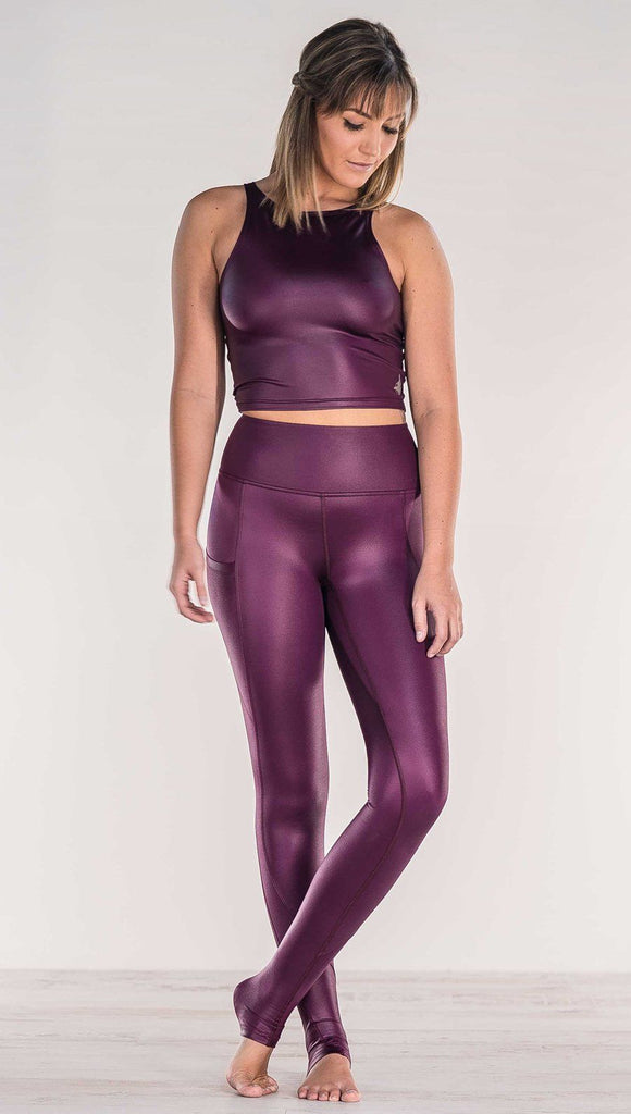 Front view of model crossing ankles wearing shiny eggplant purple colored full length leggings with right side pocket