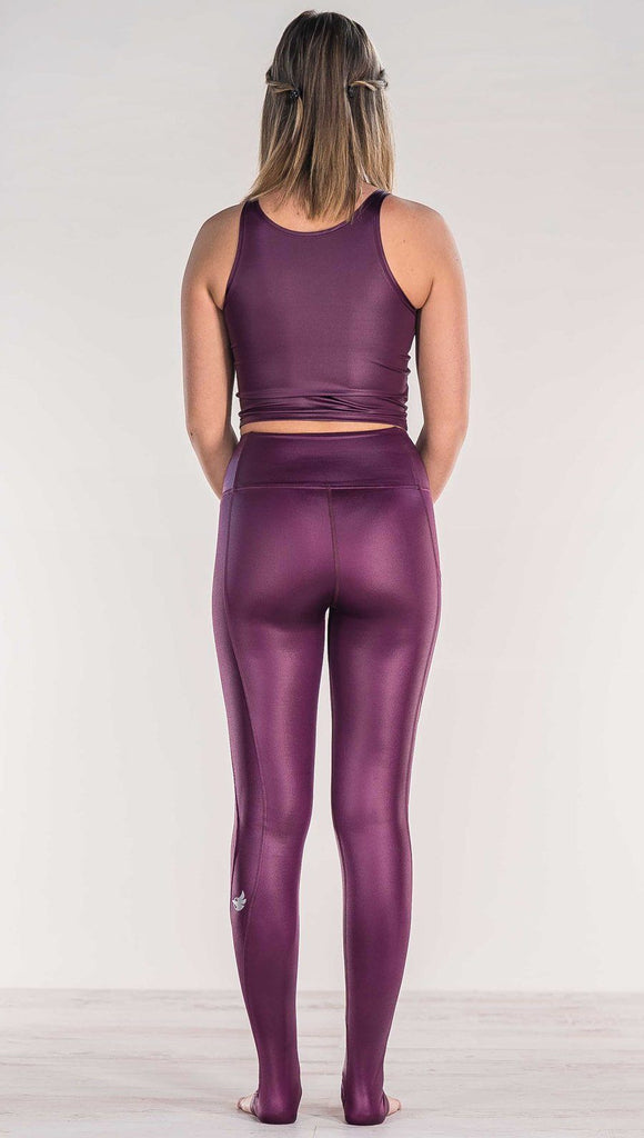 Rear view of model wearing shiny eggplant purple colored full length leggings with right side pocket