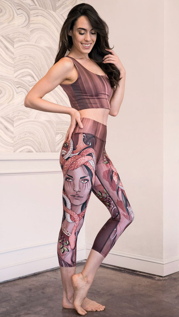 Right side view of model wearing capri leggings with a mauve color medusa head and red, white, and black snakes