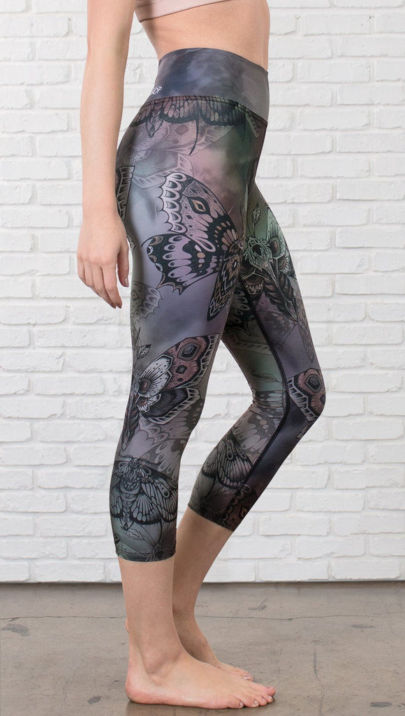 closeup right side view of model wearing capri printed leggings with gothic moths, gargoyles, skulls, ravens design