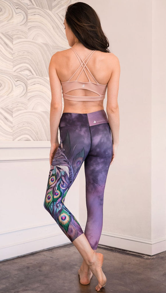 back view of model wearing peacock themed capri leggings