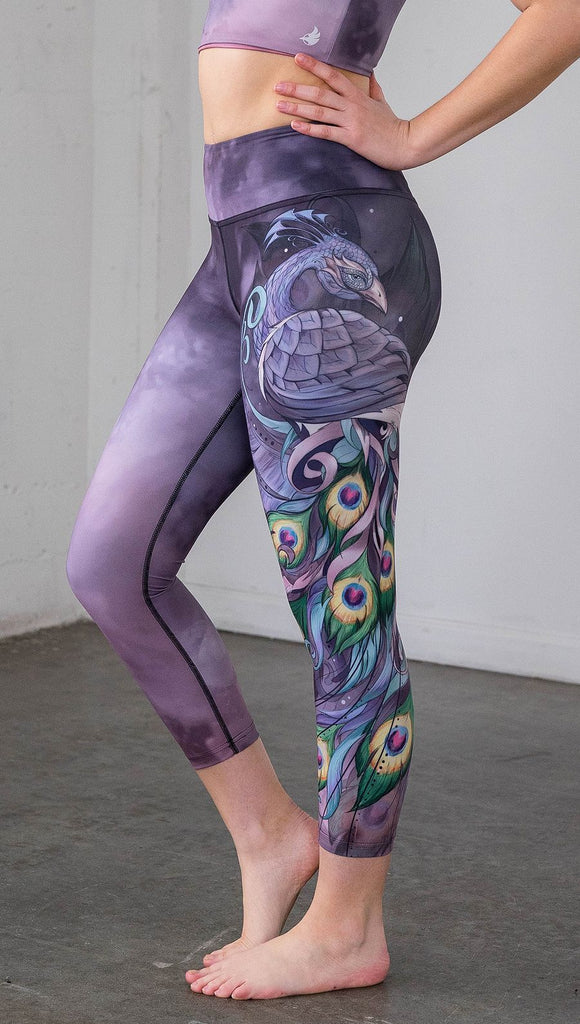 closeup left side view of model wearing peacock themed capri leggings