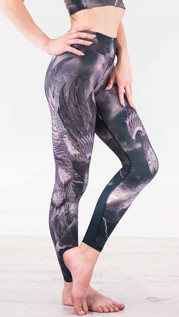 Right view of model wearing dark gray triathlon leggings with a large purple bird across the leg with lightning in the background