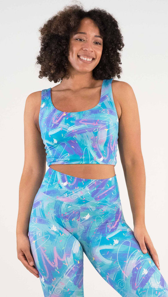 Model wearing WERKSHOP Teal/Salmon Scribble Reversible Top with whimsical brushstrokes and little confetti and eagle logos scattered throughout. (Teal on one side and Salmon on the other side)