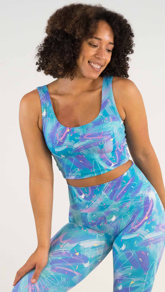 Model wearing WERKSHOP Teal/Salmon Scribble Reversible Top with whimsical brushstrokes and little confetti and eagle logos scattered throughout. (Teal on one side and Salmon on the other side)