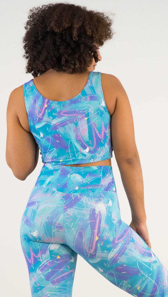 Model wearing WERKSHOP Teal/Salmon Scribble Reversible Top with whimsical brushstrokes and little confetti and eagle logos scattered throughout. (Teal on one side and Salmon on the other side)