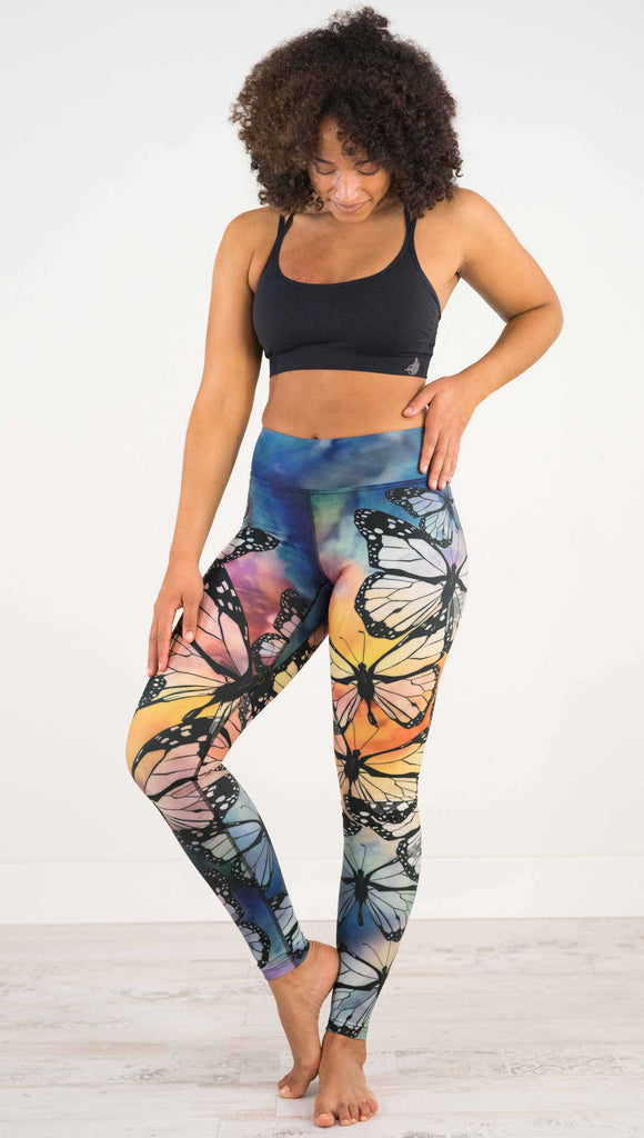 Full body, front view of model wearing WERKSHOP Butterflies Full Length Triathlon Leggings. The artwork has a kaleidoscope of rainbow colors with black outline drawings of Monarch butterflies.