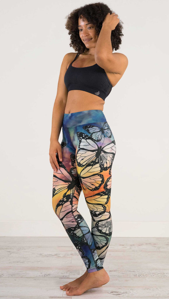 Full body side view of model wearing WERKSHOP Butterflies Full Length Triathlon Leggings. The artwork has a kaleidoscope of rainbow colors with black outline drawings of Monarch butterflies.