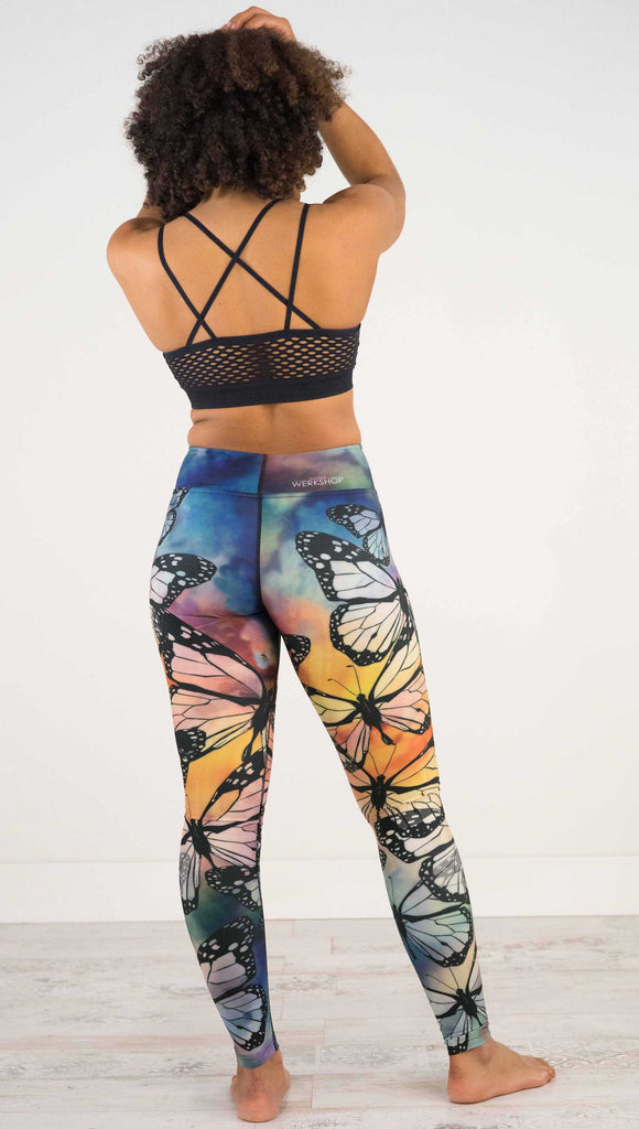 Back view of model wearing WERKSHOP Butterflies Full Length Triathlon Leggings. The artwork has a kaleidoscope of rainbow colors with black outline drawings of Monarch butterflies.