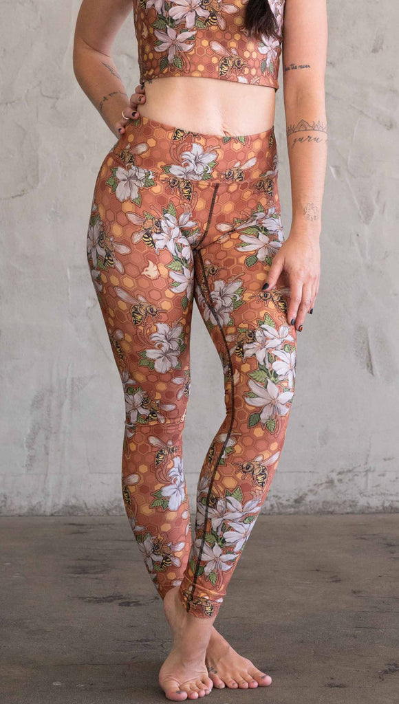 Front view of model wearing WERKSHOP Honeybees leggings in triathlon fabric. The artwork has clusters of honeybees and flowers.