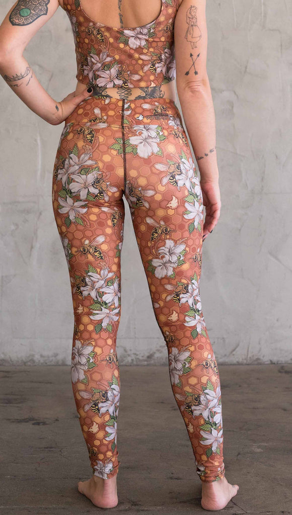 Back view of model wearing WERKSHOP Honeybees leggings in triathlon fabric. The artwork has clusters of honeybees and flowers.